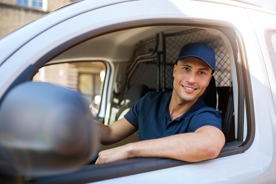 Business Insurance - Delivery Driver Leaning Out the Window of a White Van, Wearing a Matching Blue Polo Shirt and Baseball Cap